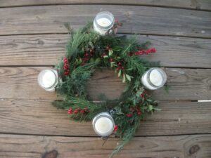 A photo of an advent wreath from above, with four white candles surrounded by a green and red wreath.