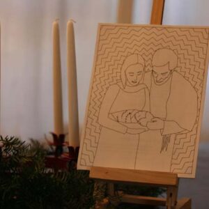 Photo of card on an easel, next to an advent wreath. The card contains an illustration of Mary and Joseph holding Jesus.