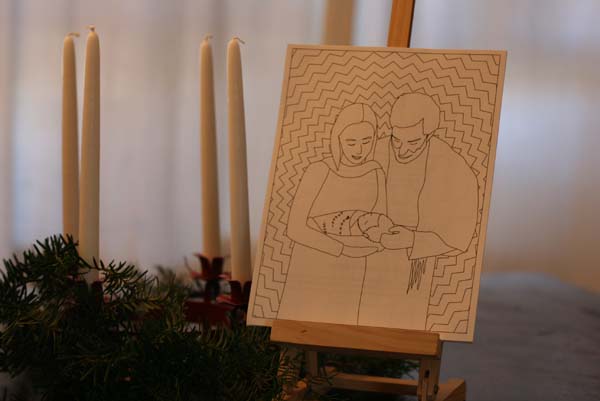 Photo of card on an easel, next to an advent wreath. The card contains an illustration of Mary and Joseph holding Jesus.
